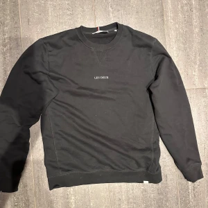 Svart sweatshirt från Les Deux - Säljer en svart sweatshirt från Les Deux med rund halsringning och diskret broderad logga på bröstet. Tröjan har långa ärmar och ribbade muddar vid ärmslut och nederkant. 