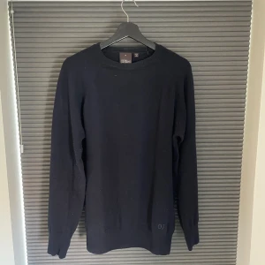 Marinblå ulltröja från Oscar Jacobson - Stickad tröja från Oscar Jacobson i mjuk ull. Rund halsringning med diskret OJ-brodyr vid nederkanten. Storlek L funkar för M också.