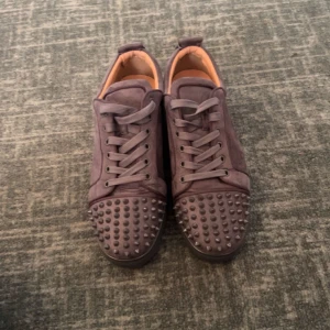 Christian Louboutins Gråa - Säljer ett par mörklila sneakers med coola nitar framtill. Skorna har snörning och är gjorda i mocka med en platt sula. Perfekta för dig som vill sticka ut med din stil.  Dåliga bilder, kom pm för bättre bilder.