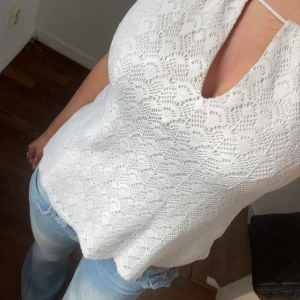 Vit spetslinne med nyckelhålsringning - Säljer ett vitt linne med spets och vacker nyckelhålsringning framtill. Toppen har smala axelband och är ärmlös, perfekt för varma dagar. Snyggt mönster i spets ger en romantisk känsla.