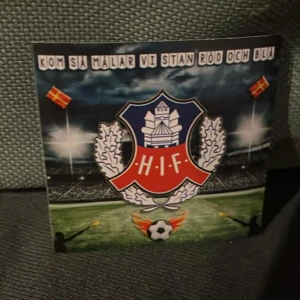 Helsingborg klistermärken 200 st - Klistermärken  Helsingborgs IF:s klubbmärke på omslaget, dekorerad med två skånska flaggor och en fotbollsplan i bakgrunden. Texten 'Kom så målar vi stan röd och blå' syns högst upp. Perfekt för HIF-fans.