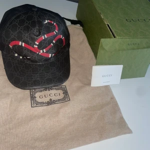 Svart Gucci Kingsnake keps - Säljer min Gucci keps i storlek M då jag inte använder den längre, du får påsen boxen och resterande papper. Kepsen är i perfekt skick, inga tecken på slitage. Kontakta vid fler bilder eller funderingar.