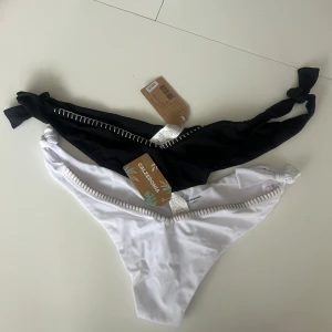 Svart och vit bikiniunderdel med knyt  - Två nya bikiniunderdelar från Calzedonia i svart och vitt. Båda har knyt i sidorna och dekorativt band med sicksack-detalj framtill. Snygg och enkel design, perfekt för stranden eller poolen. Dem är aldrig använda och har prislapp kvar!