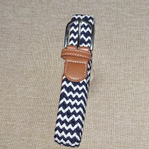 Randigt bälte med läderdetaljer - Snyggt bälte med svart och vitt zickzackmönster och bruna läderdetaljer vid spännet. Bältet har ett klassiskt metallspänne och passar perfekt för att ge outfiten en cool touch.