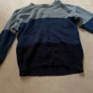 Randig stickad tröja från H&M - Säljer en stickad tröja från H&M i storlek S. Tröjan har breda horisontella ränder i ljusgrått, blått och mörkblått. Perfekt för dig som gillar en avslappnad och mysig stil. Har ett litet hål på högra armbågen men den syns knappt!