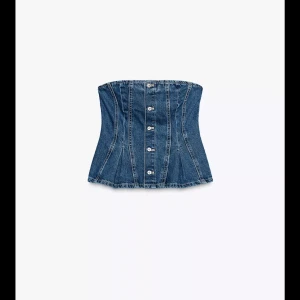 Jeans korsett-topp med knappar - Snygg jeans korsett-topp i blå denim med knappar framtill. Toppen är axelbandslös och har en figurnära passform som framhäver midjan. Perfekt att styla med kjol eller byxor för en trendig look.