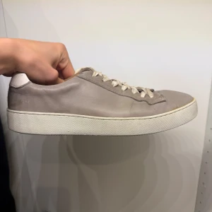 Tiger of sweden skor!  - Säljer ett par stilrena beige sneakers med snörning och platt sula. Skorna har en minimalistisk design och är tillverkade i skinn med vita skosnören och sula. Perfekta för en clean och avslappnad look.