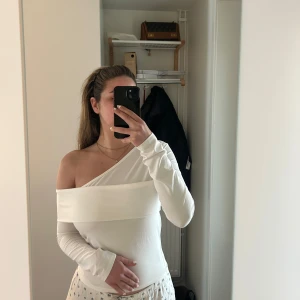 Vit offshoulder långärmad topp - Säljer en vit långärmad topp med offshoulder-design. Tröjan har en bred kant upptill som ger en snygg och modern look. Använd 2 gånger. 