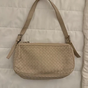 Beige axelväska med flätad design - Säljer en beige axelväska med snygg flätad struktur och dragkedja upptill. Väskan har en enkel och stilren look med justerbart axelband. Perfekt för att lyfta din outfit med en trendig accessoar.