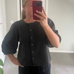 Svart blus med puffärmar och knappar - Säljer denna svarta/grå jeans blusen med puffärmar från Lindex! 