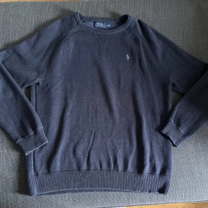 Mörkblå stickad tröja från Polo Ralph Lauren - Säljer en klassisk mörkblå stickad tröja från Polo Ralph Lauren med rund halsringning och diskret broderad logga på bröstet. Tröjan har långa ärmar och ribbade muddar vid ärmslut och nederkant. Perfekt för en stilren look. Den är i ett jättebra skick och inga defekter alls. Skick: 9,5/10. Nypris: Ca 1400-1500