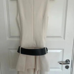 Beige klänning med svart bälte från Zara - Säljer en stilren beige klänning från Zara med markerad midja och svart bälte. Klänningen är ärmlös och har en figurnära passform med lätt utställd kjol. 