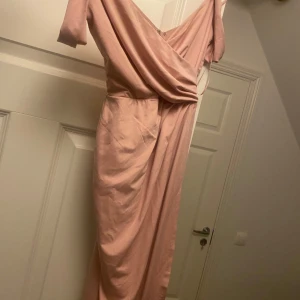 Ljusrosa långklänning från Nelly Eve - Säljer en elegant ljusrosa långklänning från NLY Eve. Klänningen har omlottliv, v-ringning och draperad detalj framtill. Perfekt för bal eller festliga tillfällen. Materialet känns mjukt och har ett fint fall.