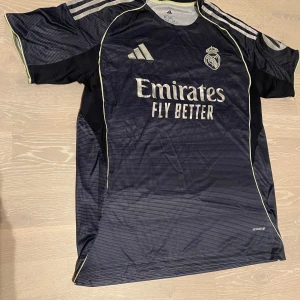 Svart Real Madrid T-shirt 25/26 - •Säljer en jätte fin 25-26 svart/marinblå Real Madrid T-shirt.  •Den är inte använd bara testad, jätte bra skick och inga fläckar eller hål.  •Och det är storlek M och måtten finns på dem sista bilderna •Priset kan diskuteras och skickar inom 24 Tim 💨😊