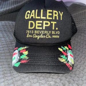 Gallery Dept svart keps med tryck - Svart truckerkeps från Gallery Dept med stor gul text framtill och adressen till Beverly Blvd, LA. Skärmen har färgglada penseldrag i rött, grönt, gult och vitt som ger en unik vibe. Baksidan är i mesh för extra ventilation. Perfekt för dig som gillar streetwear och statement-plagg.