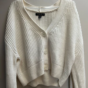 Vit stickad kofta från Amisu - Superfin vit stickad kofta från Amisu med v-ringning och stora knappar framtill. Modellen är croppad och har långa ärmar samt breda ribbade muddar. Perfekt att slänga över en topp för en chill look.