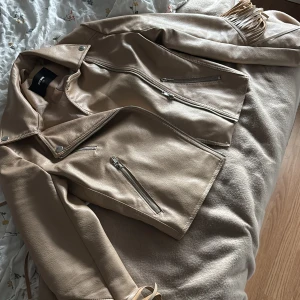Beige skinnjacka med fransar Bik Bok XS - Snygg beige skinnjacka från Bik Bok i storlek XS. Jackan har coola fransdetaljer längs ryggen och ärmarna, flera silvriga dragkedjor.  Så fin verkligen!!!