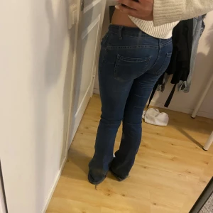 Blå bootcut jeans med låg midja - Snygga blå jeans med bootcut passform och låg midja. Klassisk femficksmodell med dragkedja och knapp framtill. Jeansen har en mörkblå ton och är tillverkade i mjukt denim-material som sitter skönt. Perfekta för dig som gillar retrovibbar och vill ha ett par jeans med lite utsvängda ben.