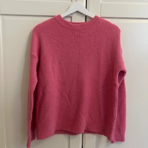 Rosa stickad tröja med rund hals - Mysig rosa stickad tröja med rund halsringning och långa ärmar. Tröjan har en enkel design med ribbade muddar vid ärmslut och nederkant, perfekt för lager-på-lager under kyliga dagar.