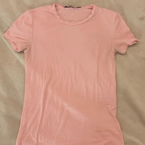 Ljusrosa t-shirt från 157 XS - Snygg ljusrosa t-shirt från 157 i storlek XS. Modellen är klassisk med rund hals och korta ärmar, perfekt för en chill och enkel look. Materialet är mjukt och skönt bomull som sitter slim mot kroppen. Passar dig som gillar stilrena och basic plagg.