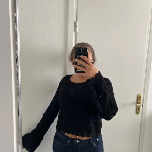 Svart stickad croppad tröja från Vila - Svart stickad tröja från Vila med snyggt hålmönster och croppad passform. Tröjan har långa ärmar och vågig kant nertill för en extra detalj. Perfekt att styla med jeans eller kjol för en trendig look.