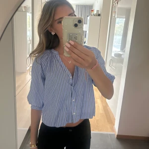 Blåvit randig blus/skjorta - Säljer en blå och vit randig skjorta med knappar framtill och trekvartsärm. Skjortan har en avslappnad passform och är perfekt för en fräsch och somrig look. Tillverkad i mjuk bomull som känns skön mot huden.