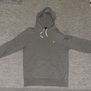 Grå hoodie från Polo Ralph Lauren - Säljer en stilren grå hoodie från Polo Ralph Lauren med klassisk vit logga på bröstet.
