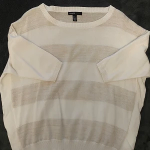 Randig vit stickad tröja Mango - Säljer en vit stickad tröja från Mango med diskreta breda ränder i ljusbeige. Tröjan har rund halsringning, ribbade muddar och lång ärm. Perfekt för lager-på-lager och chill dagar.