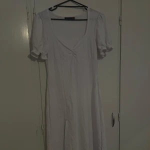 Vit långklänning från Boohoo - Supersöt vit långklänning från Boohoo med puffiga korta ärmar och v-ringning. Klänningen har en lätt rynkad detalj vid bysten och är gjord i ett mjukt bomullsliknande material. Perfekt för sommarens alla tillfällen!