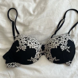 Svart spets-bh från Intimissimi - Snygg svart bh från Intimissimi med vit broderad spets upptill och längs kanterna. Kuporna är vadderade och har justerbara axelband. Perfekt för dig som gillar en feminin och elegant look med extra detaljer.