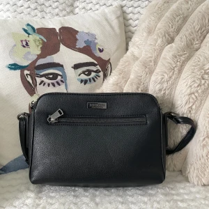 Svart axelväska från Don Donna - Snygg svart axelväska från Don Donna i stilren design. Väskan har justerbar rem, silverfärgade dragkedjor och en praktisk ytterficka framtill. Tillverkad i slätt skinnliknande material och rymmer det viktigaste för dagen. Pris kan diskuteras💗