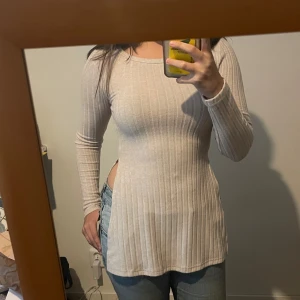 Beige ribbad långärmad topp - Säljer en beige ribbad långärmad topp med rund hals och slim fit. Toppen har slitsar på sidorna. Materialet är mjukt och stretchigt, vilket gör den skön att bära hela dagen. Passar fint med svarta eller beiga byxor. Säljer då den är för tight för mig