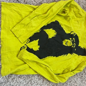 Gul långärmad t-shirt med apa - Cool långärmad t-shirt i starkt gul färg med stor svart aptryck på framsidan. T-shirten har en avslappnad passform och är gjord i mjukt bomullsmaterial, perfekt för dig som gillar att sticka ut med grafiska motiv.