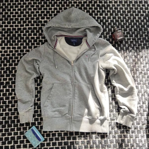 Grå GANT Zipup - Snygg grå hoodie från GANT i bomull med dragkedja och huva. Tröjan har ribbade muddar, snörning i huvan och klassisk GANT-logga broderad på bröstet. Fodret i luvan har en stilren randig detalj i rött, vitt och blått. Some signs if wear as shown in the pictures✅