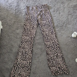 Leopardmönstrade bootcut byxor - Säljer ett par snygga bootcut byxor med leopardmönster i beige och svart. Byxorna har hög midja och är tillverkade i ett mjukt, stretchigt material som sitter skönt på kroppen. Perfekta för dig som vill sticka ut med en trendig look.