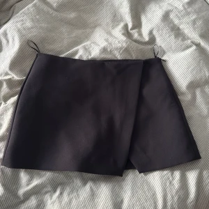 Svart omlottkjol från Zara - Stilren svart kortkjol från Zara i omlottmodell med shorts under. 