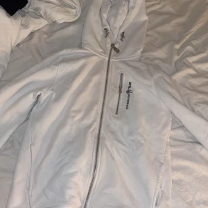 Vit hoodie från Sail Racing med dragkedja - Snygg vit hoodie från Sail Racing med hel dragkedja, huva med snörning och en bröstficka. Långärmad och i mjukt material. Storlek 160 i barnstorlek 