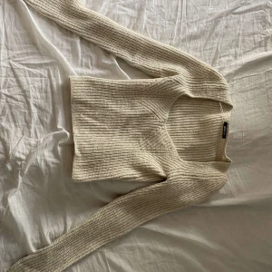 Beige stickad tröja från Gina Tricot - Supermysig beige stickad tröja från Gina Tricot med v-ringning och lång ärm. Tröjan har en ribbad struktur och är i en lite croppad modell som passar perfekt till höga jeans eller kjol. Använd fåtal gånger!