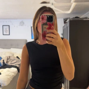 Svart ärmlös topp med öppen rygg - Säljer en svart, ärmlös topp med cool öppen rygg och rund hals. Toppen är croppad och har en snygg, tight passform som framhäver figuren. Perfekt för dig som gillar minimalistisk stil med en twist. Materialet känns mjukt och stretchigt mot huden. Aldrig kommit till användning