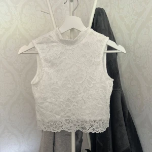 Vit spetsig linnetopp från Even&Odd - Supersöt vit ärmlös linnetopp från Even&Odd med vacker spets över hela toppen och hög hals. Perfekt att styla med jeans eller kjol för en fräsch look. Toppen har en croppad passform och fina spetsdetaljer längs nederkanten.