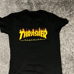 Svart Thrasher t-shirt med flames - Svart t-shirt från Thrasher med ikoniskt flames-tryck i gult och rött på bröstet. Klassisk passform och rund hals. Perfekt för dig som gillar streetwear och skatekultur.