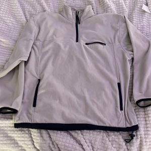 Ljusgrå fleecejacka från Mac One - Ljusgrå fleecejacka från Mac One med svart dragkedja och detaljer. Jackan har hög krage, tre fickor med dragkedja och justerbar nederkant med snörning. Perfekt för kyliga dagar och enkel att slänga på över en hoodie.