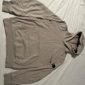 Beige hoodie från Stone Island Junior - Säljer en beige hoodie från Stone Island Junior med klassisk patch på ärmen. Tröjan har stor känguruficka framtill, huva och långa ärmar. Perfekt för dig som gillar streetwear och vill ha en clean look med exklusiv känsla. Hoodien har lite små defekter men inget tydligt. Storleken är Junior/xs-s. Tveka inte att fråga om ni undrar något eller vill ha fler bilder