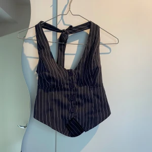 Väst med knyt i nacken - Supersnygg väst som tyvärr är förstor för mig! Den går att knyta i nacken. Västen har djup v-ringning, knappar framtill och en figurnära passform. Storleken står inte men skulle chansa på något större än S som jag oftast har. 