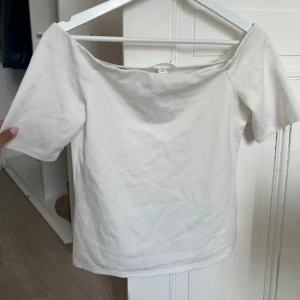 Vit offshoulder topp i bomull - Säljer en stilren vit offshoulder topp i bomull. Toppen har korta ärmar och en rak, enkel passform som ger en clean look. Perfekt att matcha med jeans eller kjol för en fräsch vibe. Superenkel att styla och passar till många olika outfits.