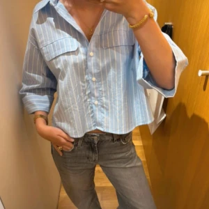 Blåvit randig skjorta med knappar - Snygg blå skjorta med vita ränder och croppad passform. Skjortan har knappar framtill, två bröstfickor och trekvartsärmar. Perfekt för en chill och trendig look. En knapp på skjortan längst upp är borta men den går fortfarande att stänga! Lånad bild💞