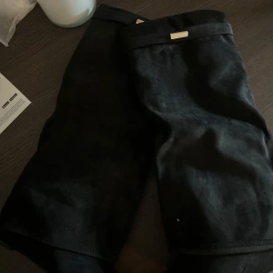 Svarta bootsi mockaimitation - Snygga svarta boots i mjuk mockaimitation med stilren design och dekorativ metallbricka. Skorna  har raka ben och känns riktigt lyxiga, perfekta för dig som vill ha en clean look med lite edge. Klacken är 8cm och är oanvända 