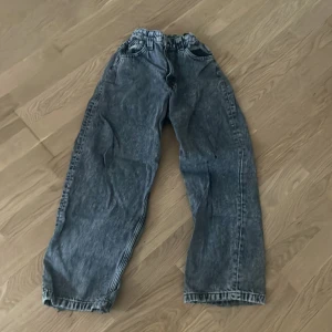 Baggy cargopants i tvättad denim - Säljer ett par baggy cargopants i tvättad blå denim med bred passform och elastisk midja. Byxorna har stora fickor på sidorna och bak, samt klassiska jeansdetaljer. Perfekt för dig som gillar streetwear och vill ha en chill look.