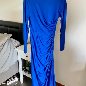 Blå långklänning från SHEIN - Snygg blå långklänning från SHEIN i mjukt och stretchigt material med 62% viskos. Klänningen har lång ärm, rund hals och coola draperade detaljer på sidan som ger en smickrande siluett. Perfekt för dig som gillar att sticka ut med färg och stil.