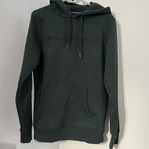 Mörkgrön Sail Racing hoodie med huva - Snygg mörkgrön hoodie från Sail Racing i storlek S. Tröjan har huva med snörning, stor magficka och diskret logga på bröstet. Tillverkad i mjuk bomullsmix, perfekt för chill dagar. Långärmad och loose fit för skön stil. Pris diskuteras